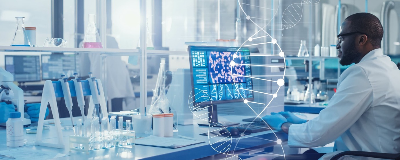 A life sciences manufacturing worker wearing glasses and a white lab coat sitting at a computer.