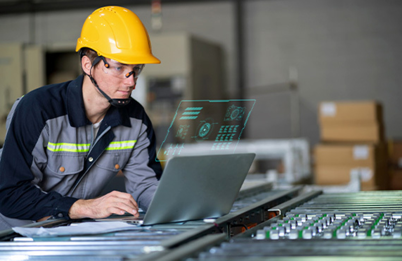 A factory employee engaged with a laptop, emphasizing cybersecurity measures in the integration of OT and IT systems.
