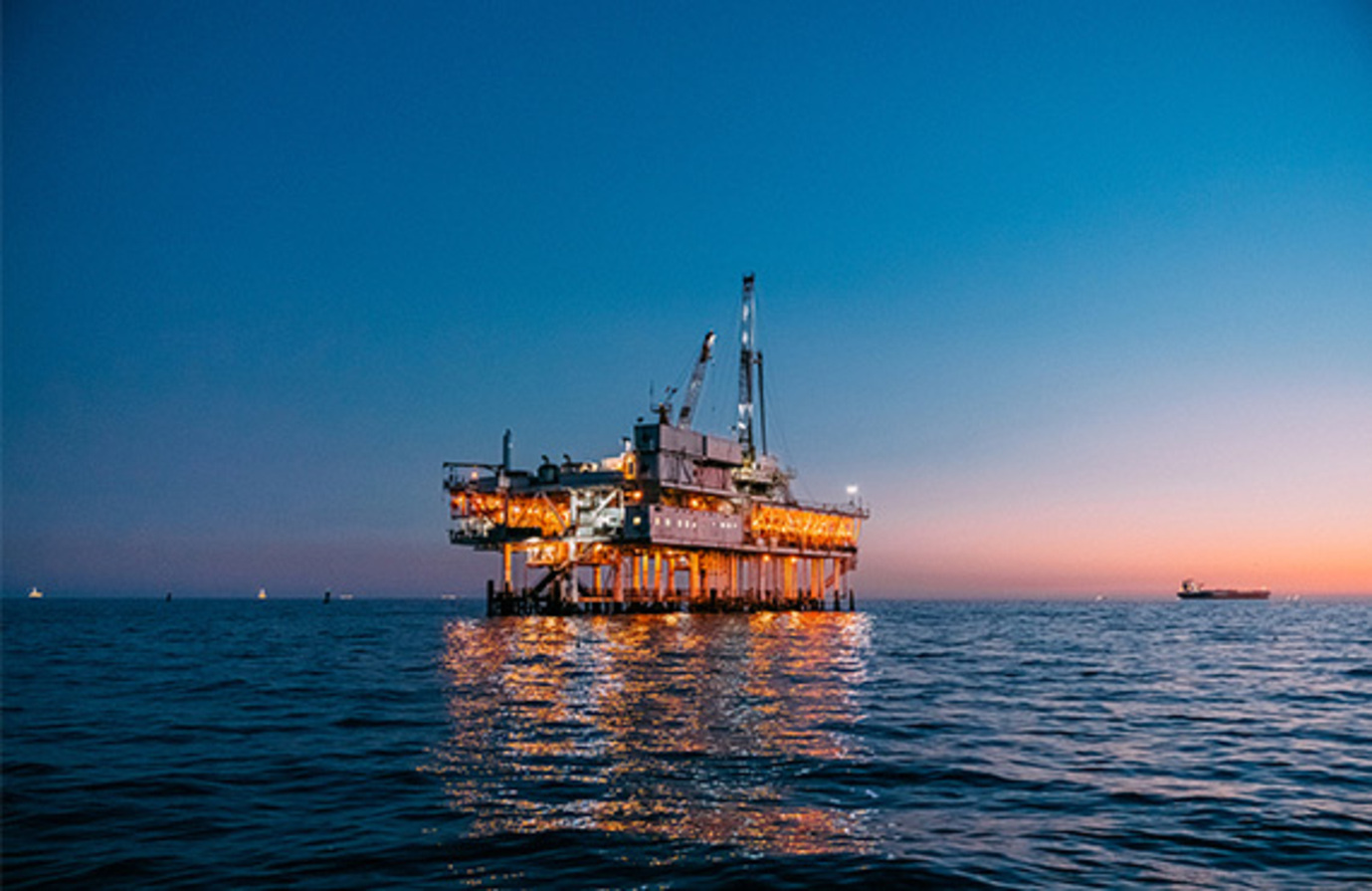 An oil rig silhouetted against a dusky ocean backdrop, emphasizing the need for advanced safety in offshore platforms.