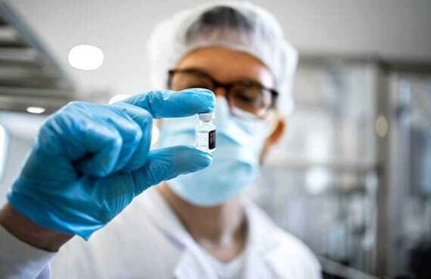 Batch processing software used to create a vaccine held in a vial by a pharmaceutical worker in protective equipment.