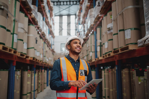 A warehouse worker using ProofCheck surrounded by boxes with a happy expression.