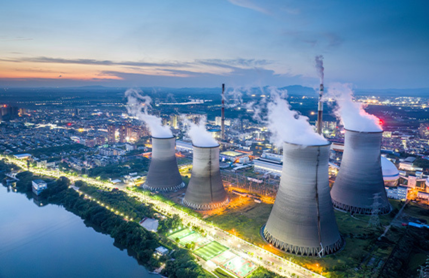 Dusk view of an industrial cooling tower, highlighting the need for cybersecurity in steam power facilities.