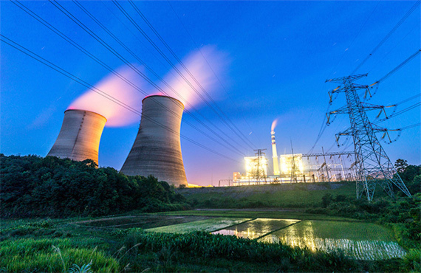 Image shows a nuclear energy power plant at sunset with cooling towers emitting clean steam