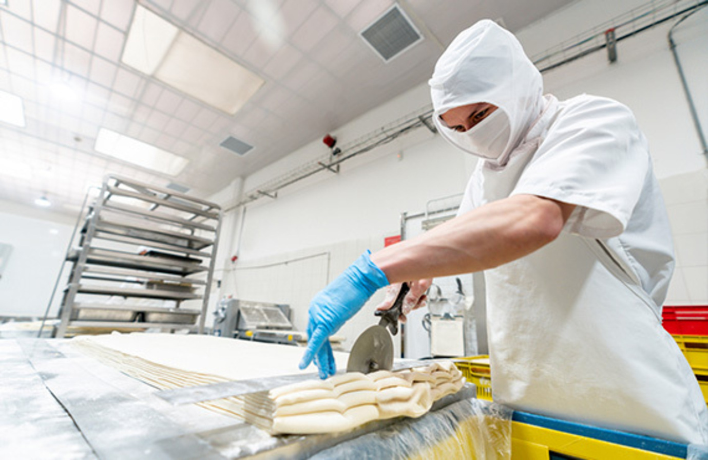 A dedicated worker checks the quality of bread in a factory, highlighting food and beverage manufacturing standards.