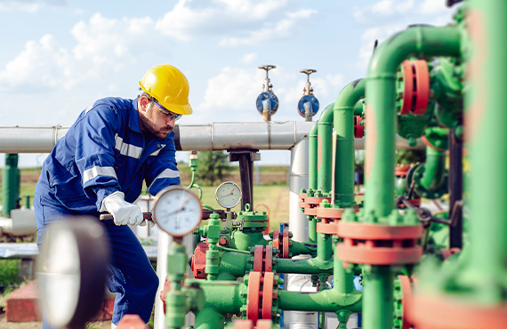 An engineer works on a factory pipe at oil refiner, ensuring valve and control devices are properly set for safety.