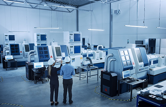 Two individuals standing in front of a large machine, strategizing for a manufacturing cybersecurity roadmap