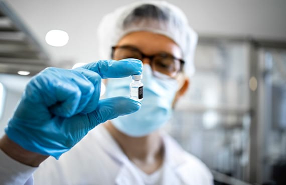 Batch processing software used to create a vaccine held in a vial by a pharmaceutical worker in protective equipment.