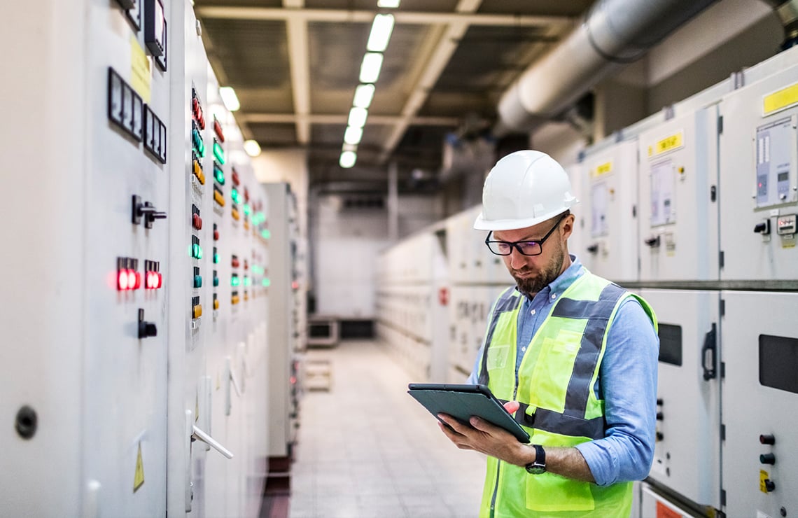 An engineer in a hard hat is checking digital twin software on a tablet