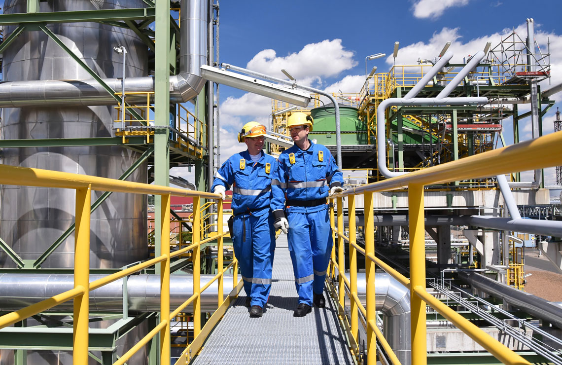 Workers on a catwalk inspecting the outside of an oil refinery
