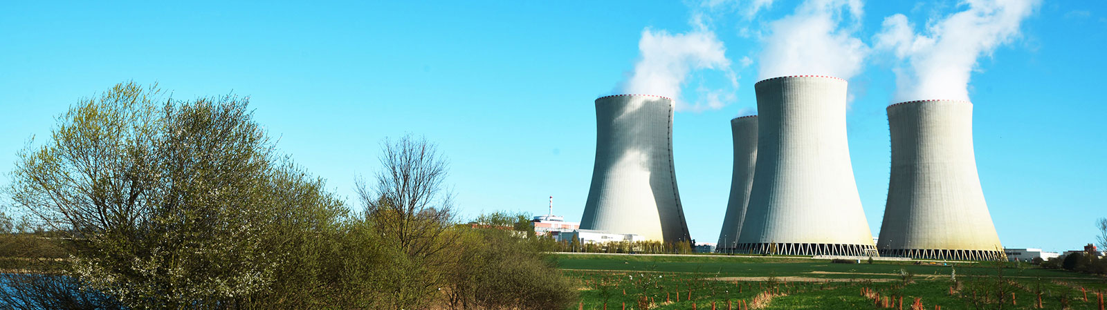 Image of a nuclear energy power plant against a blue sky with green fields in the foreground.